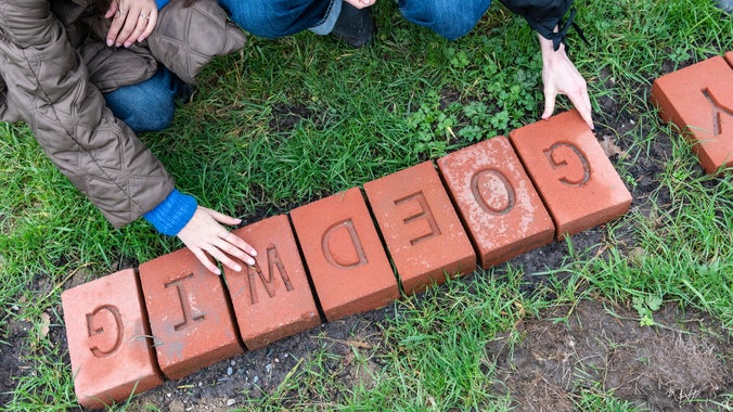 Two individuals placing engraved bricks on the grass in the Commemorative Woodland, Erddig.